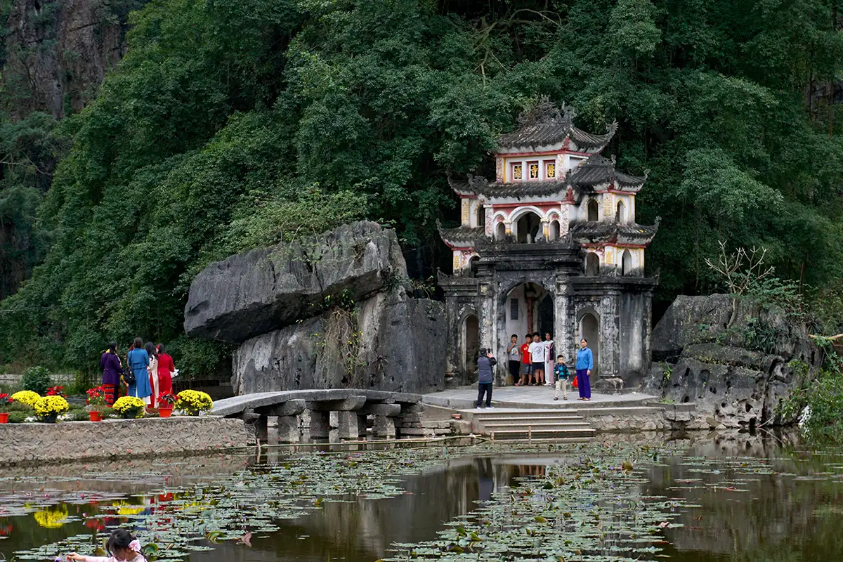 Visitors exploring Bich Dong Pagoda beside a lotus pond and limestone cliffs