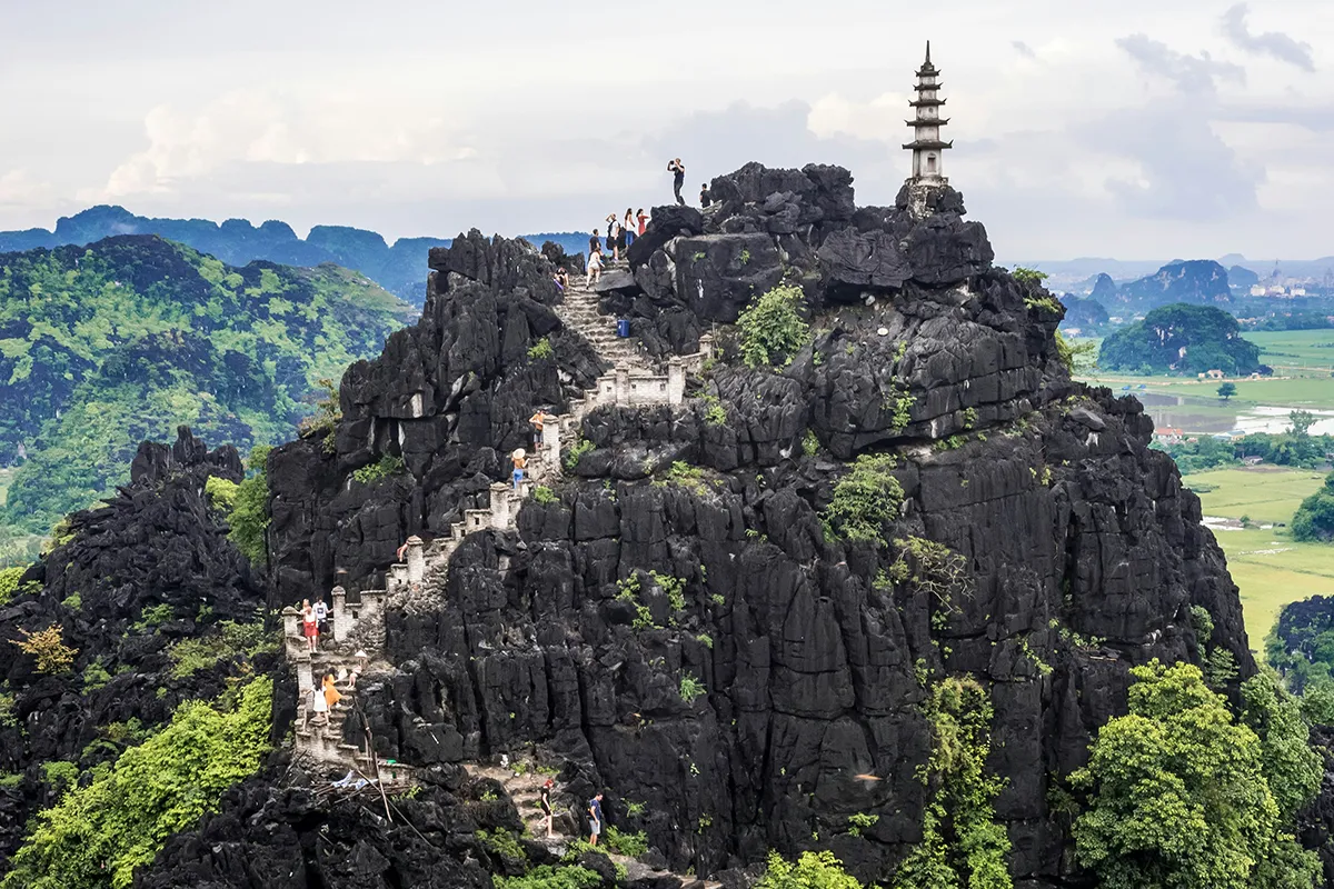 Mua Cave hiking guide featuring hikers on the steep rocky trail to the viewpoint