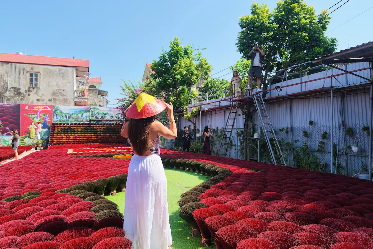 Woman posing among red incense bundles at Quang Phu Cau incense village