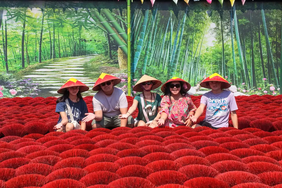Group of visitors posing among red incense bundles in Quang Phu Cau