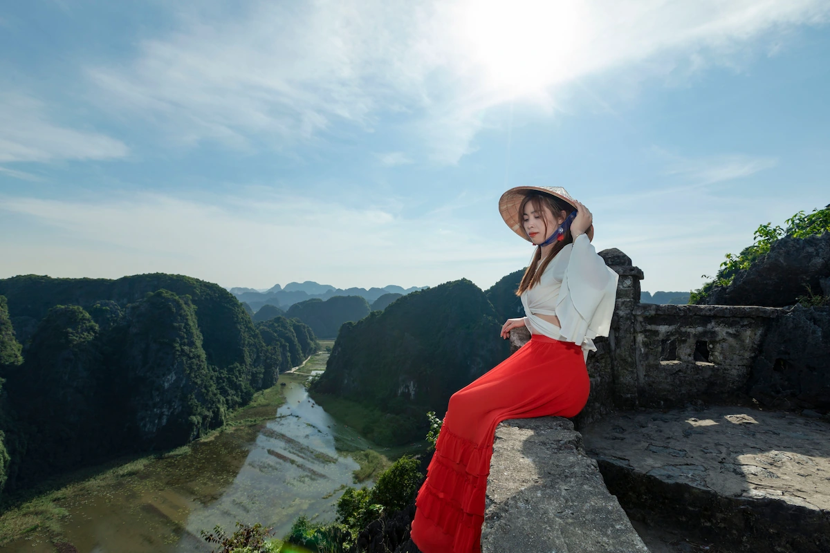 Woman in traditional Vietnamese dress overlooking Tam Coc valley from Mua Cave