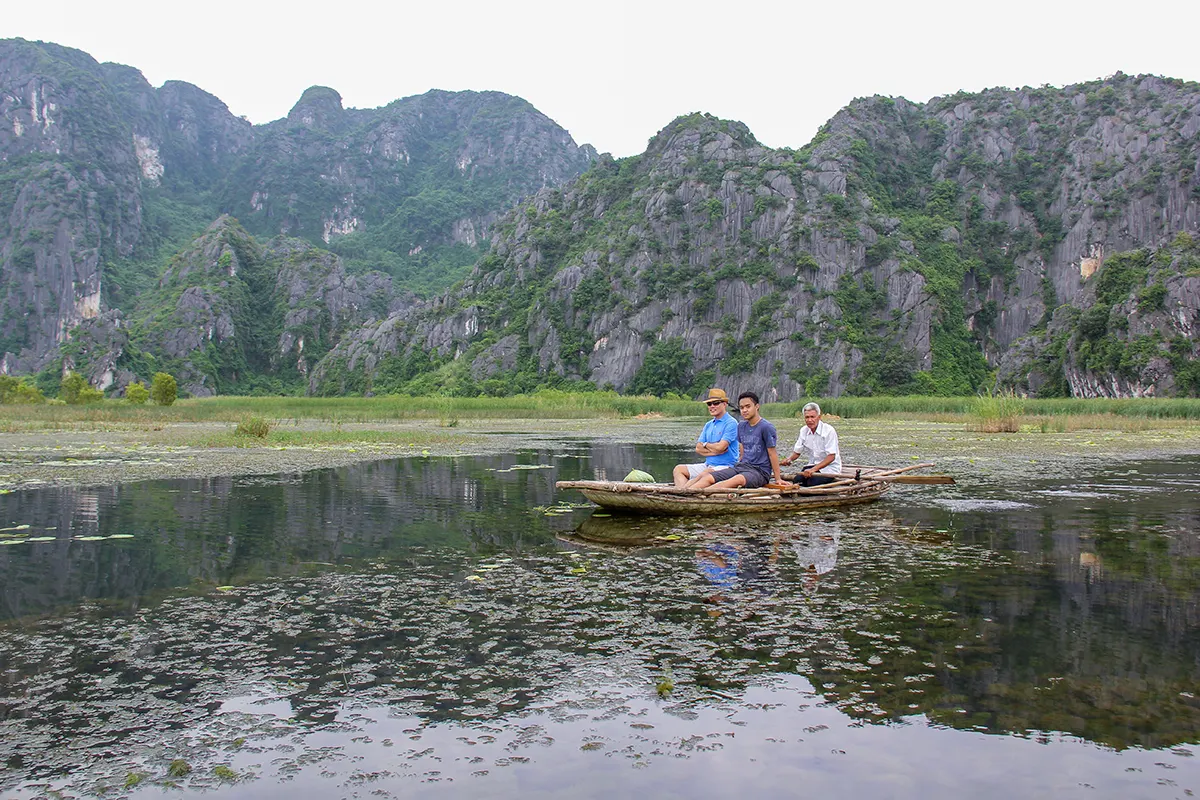 Visitors on a small boat surrounded by limestone mountains at Van Long Wetland