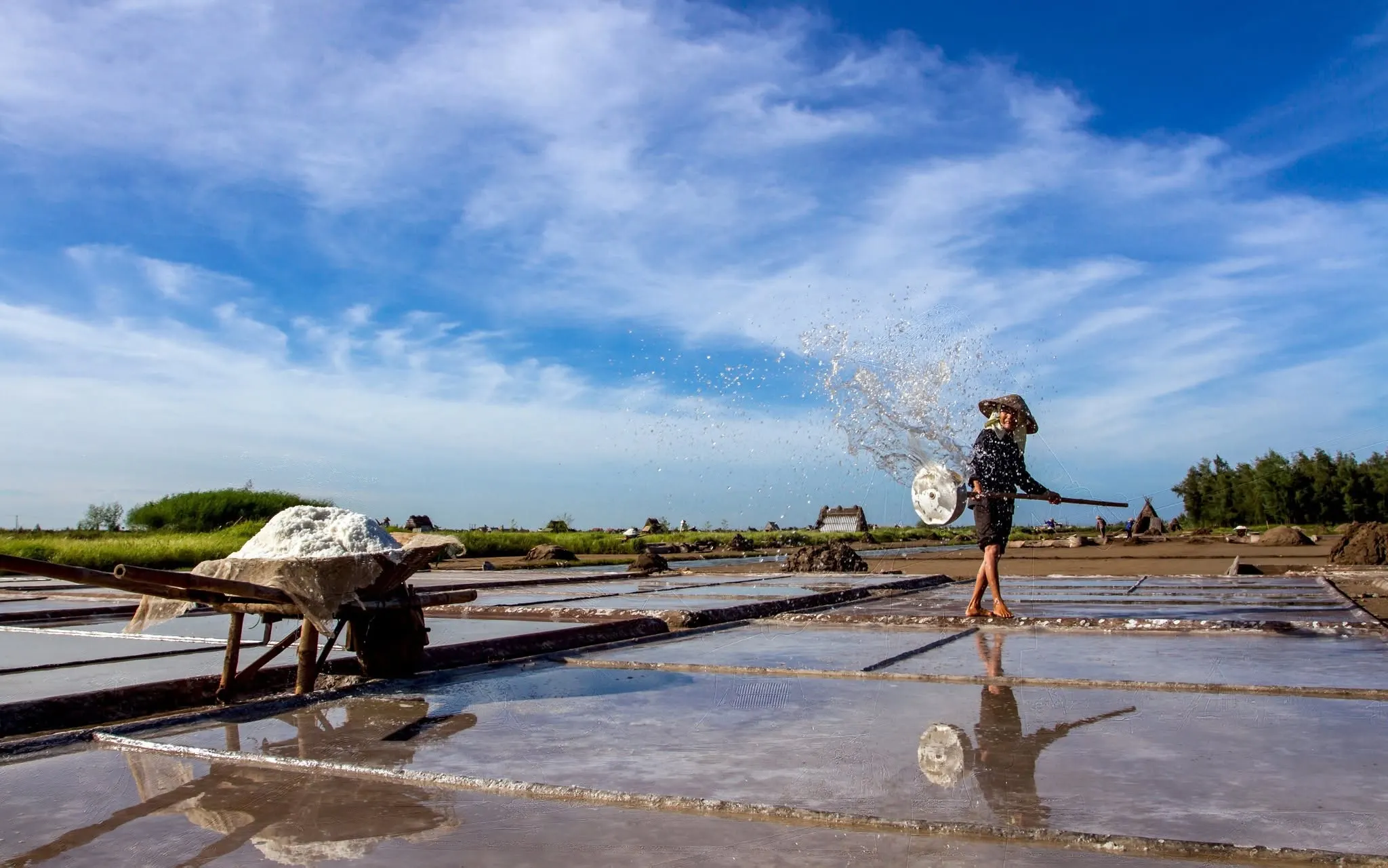 Salt farmer carrying harvested salt across the Bach Long salt fields