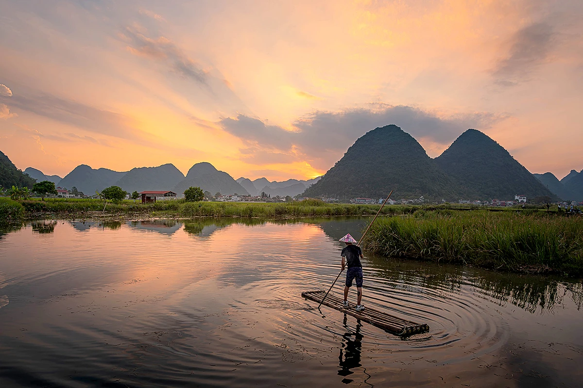 Local fisherman on a bamboo raft against limestone mountains at sunset in Ninh Binh