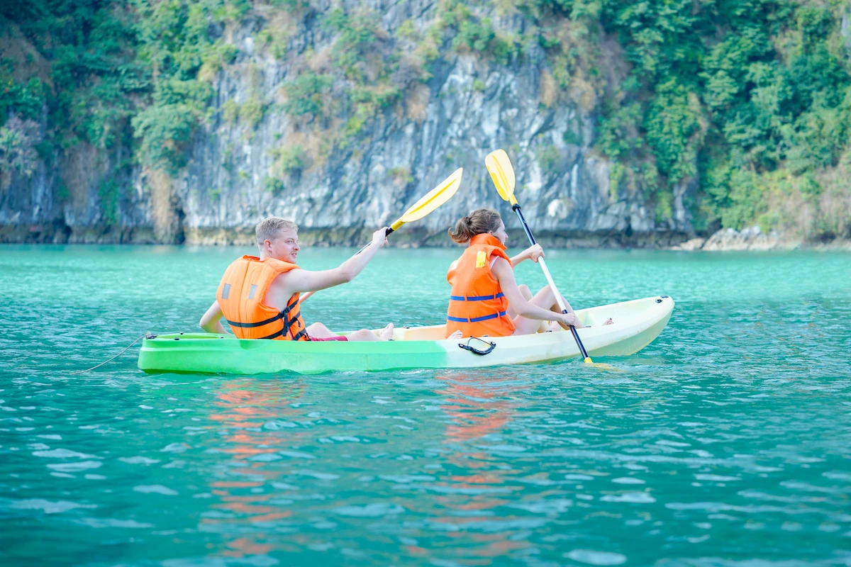 Couple paddling a kayak across turquoise water beneath limestone cliffs