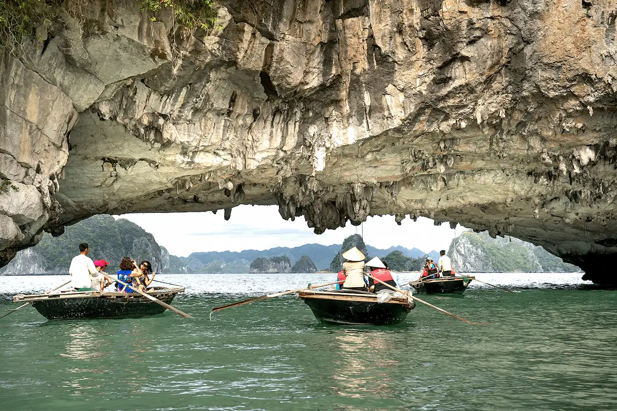 Traditional wooden boats pass beneath a limestone cave in Lan Ha Bay