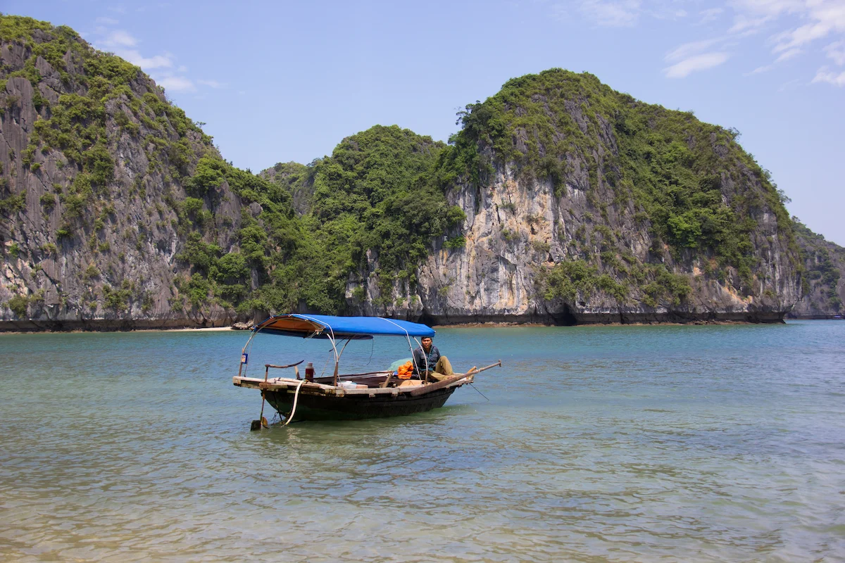 A wooden boat floats on shallow water beneath green limestone cliffs