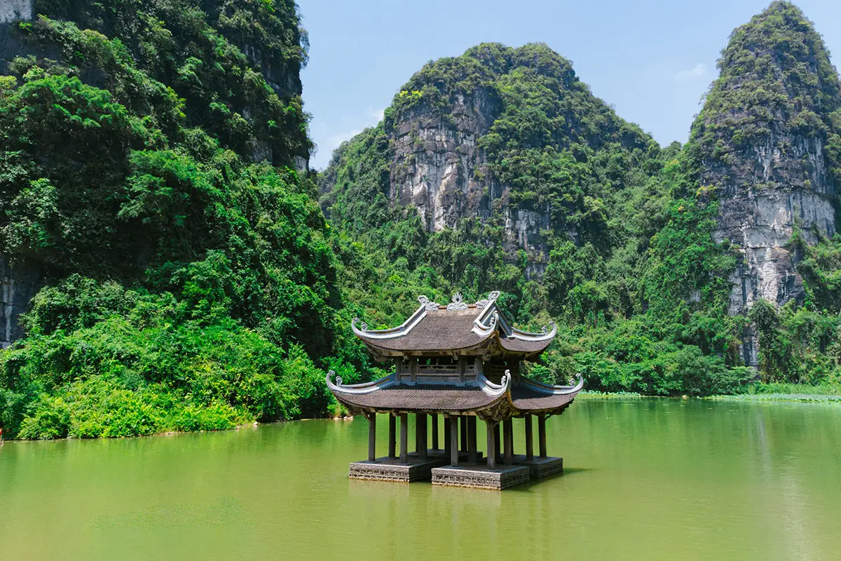 Traditional temple pavilion on green water surrounded by limestone mountains in Trang An